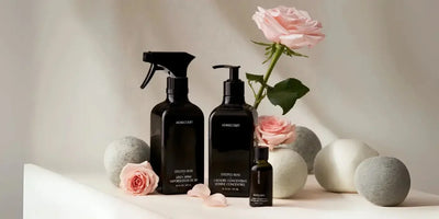 Front view of laundry concentrate in sleek black bottles with pump and spray, styled with pink roses and neutral stone props