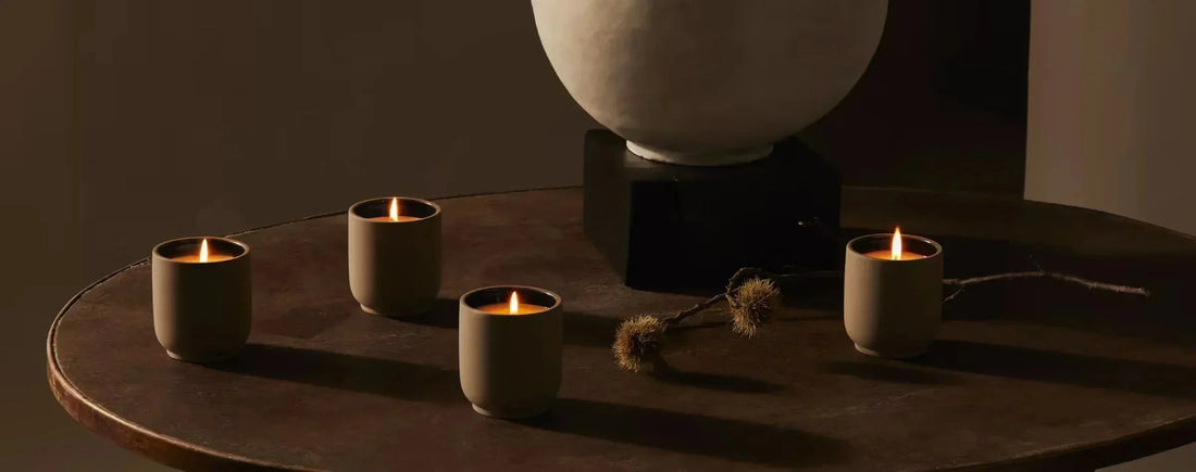Four lit ceramic votive candles glowing on a round dark wood table beside a stone urn in warm low lighting