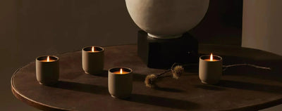 Four lit ceramic votive candles glowing on a round dark wood table beside a stone urn in warm low lighting