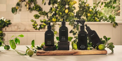 Front view of neroli leaf hand care set: matte black hand cream, hand wash, surface cleaner, and spray on a wooden tray with citrus branches