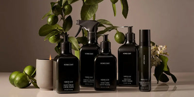 Front group view of Homecourt Neroli Leaf dish soap and matching hand wash, hand cream, surface cleaner, and room deodorizer in black bottles, styled with limes, blossoms, a lit candle