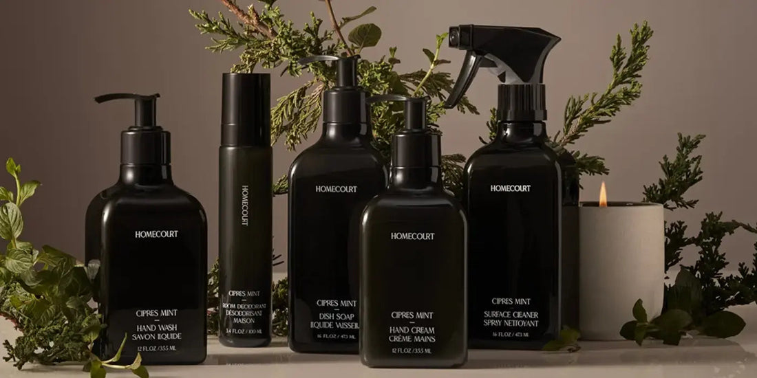 Front view of Homecourt Cipres Mint bottles: hand wash, dish soap, hand cream, and surface spray with greenery and candle
