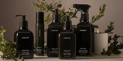 Front view of Homecourt Cipres Mint bottles: hand wash, dish soap, hand cream, and surface spray with greenery and candle