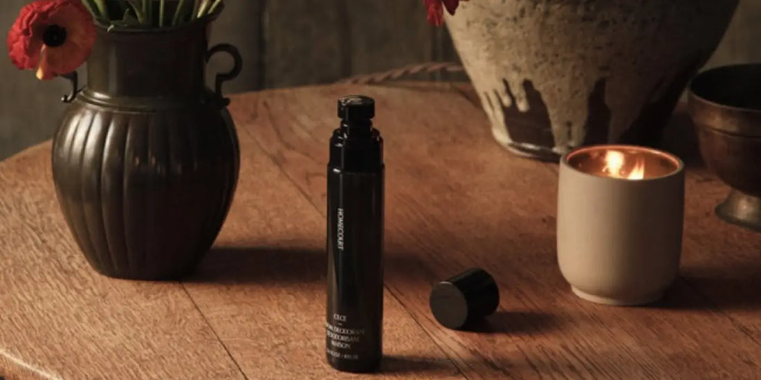Luxury room deodorant black spray bottle on a wood table beside a lit candle and dark vase with red poppies.
