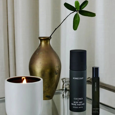 Homecourt Cocomoi natural body mist and perfume oil displayed with a lit candle & decorative vase on a glass table