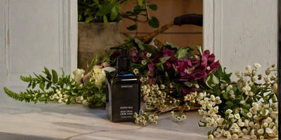 Rich hand cream steeped rose in pump bottle displayed with white baby's breath and burgundy florals