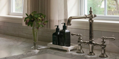 Bright kitchen sink with non-toxic dish soap bottle on a marble counter by a window.
