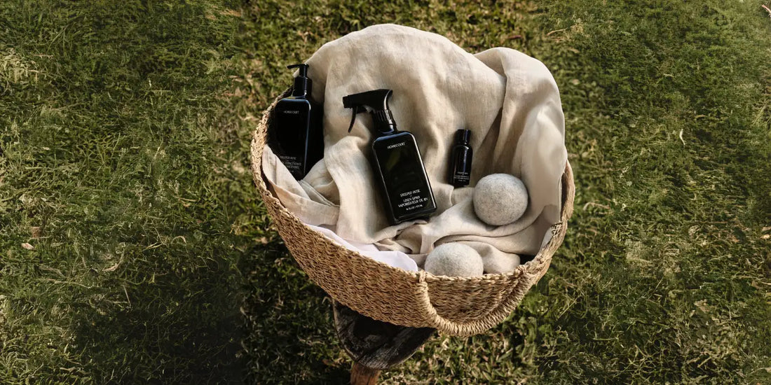 Plant-Based Home Cleaning products displayed in a woven basket with wool dryer balls on a grassy background.