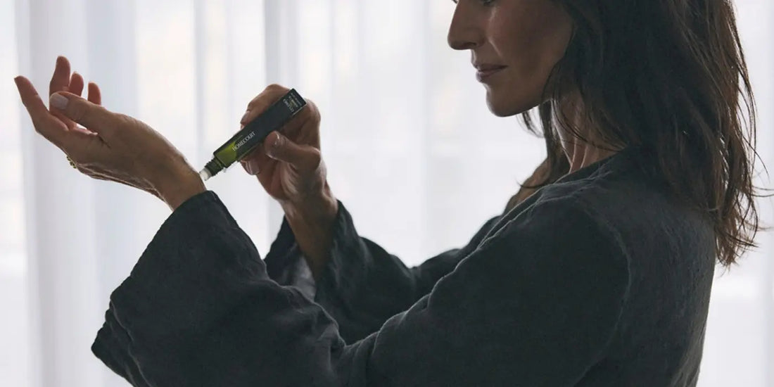 Oil-based perfume by Homecourt being applied to a woman's wrist from a rollerball tube in a soft, natural light setting