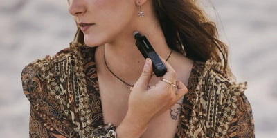 Roll-on fragrance by Homecourt being applied to the neck pulse point by a woman in a bohemian paisley blouse outdoors