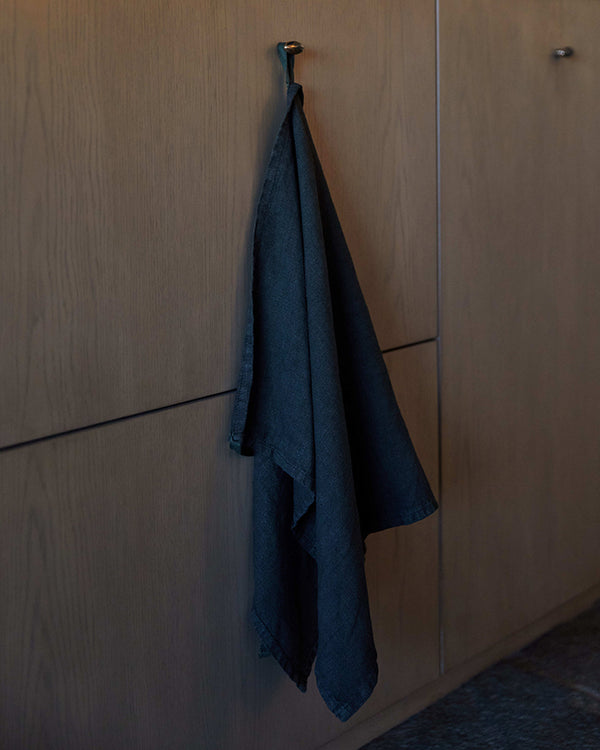 Blue linen robe hanging from a hook on a wooden wall.