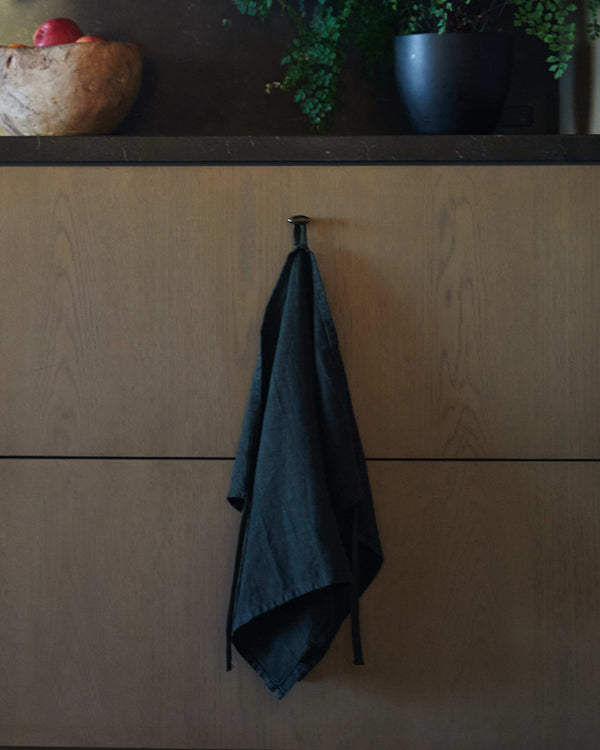 Navy blue linen robe hanging from a hook on a wooden cabinet.