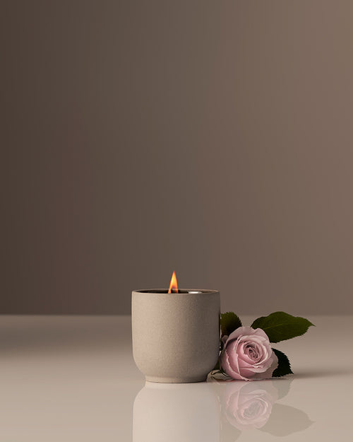 Rose candles in a minimalist beige jar beside a soft pink rose.