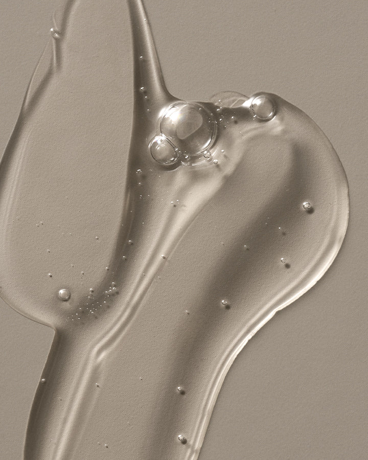 Moisturizing body wash texture with clear, gel-like consistency and air bubbles spread across a neutral surface