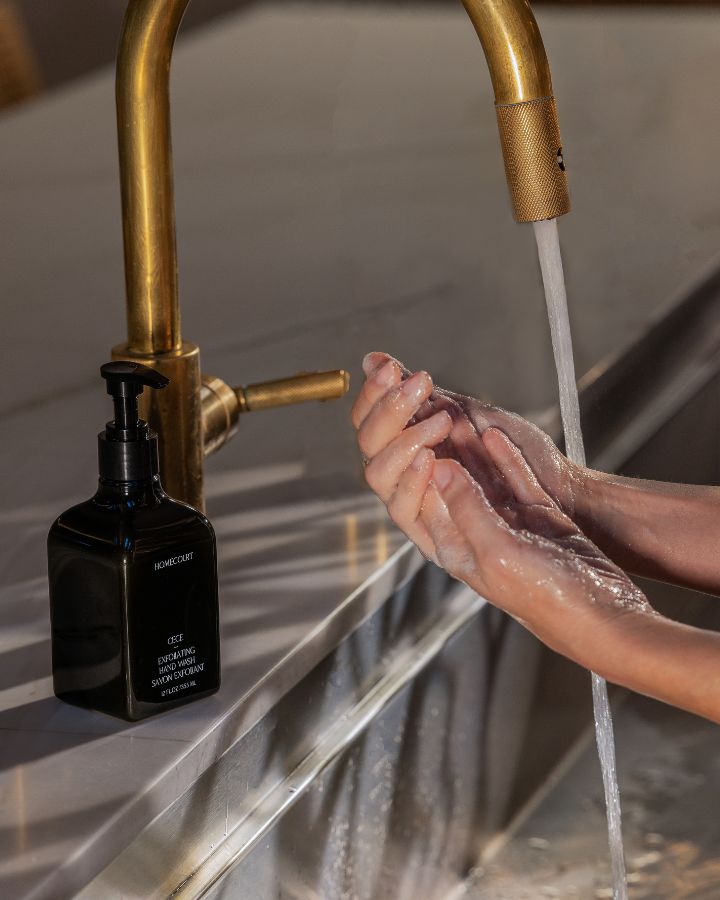Homecourt Exfoliating Hand Wash bottle beside a faucet with hands lathered in soap