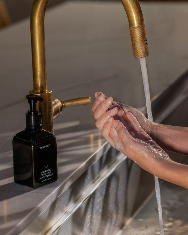 Homecourt Exfoliating Hand Wash bottle beside a faucet with hands lathered in soap