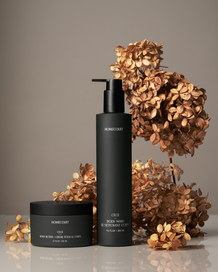 Two black skincare bottles with pump and jar on a gray background with dried flowers.