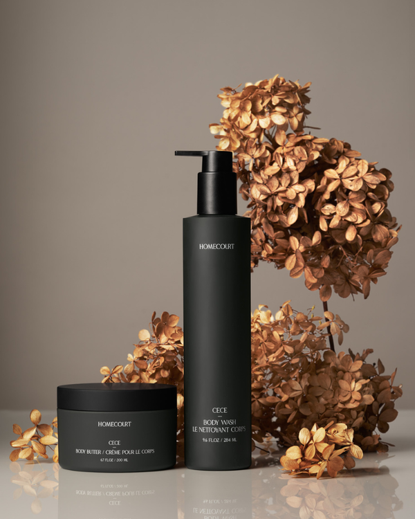 Two black skincare bottles with pump and jar on a gray background with dried flowers.