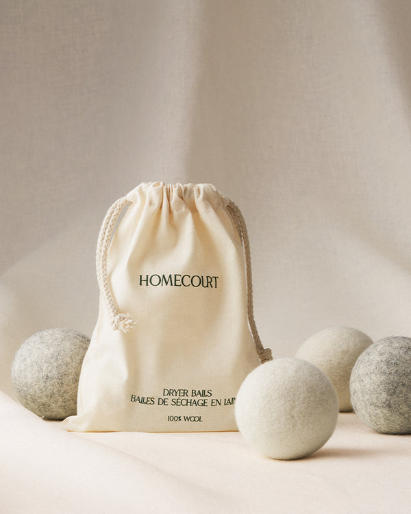 Wool dryer balls in a cotton drawstring bag surrounded by soft, neutral-toned felt balls for sustainable laundry care.