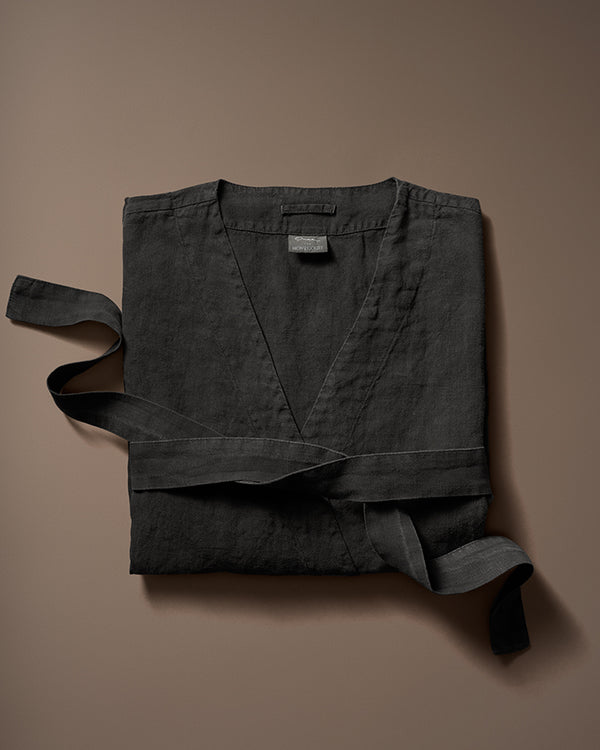 Black linen robe neatly folded with matching belt on a brown background.
