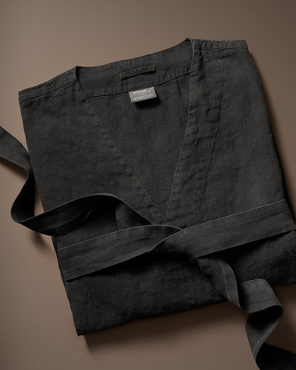 Linen black robe neatly folded with matching belt on a brown background.