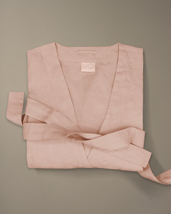 Pink linen robe folded with matching belt on a neutral beige background.