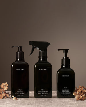 Homecourt Exfoliating Kitchen Trio in Cece fragrance, featuring Dish Soap, Surface Cleaner, and Exfoliating Hand Wash in black bottles arranged on a stone surface with dried florals against a warm neutral backdrop.