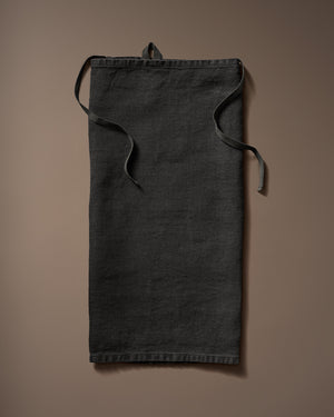 Black linen robe laid flat with waist ties on a brown background.
