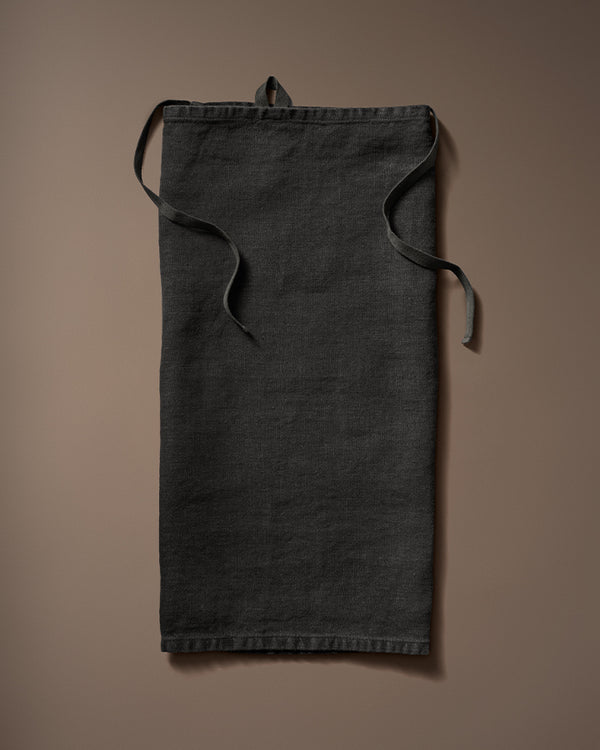 Black linen robe laid flat with waist ties on a brown background.