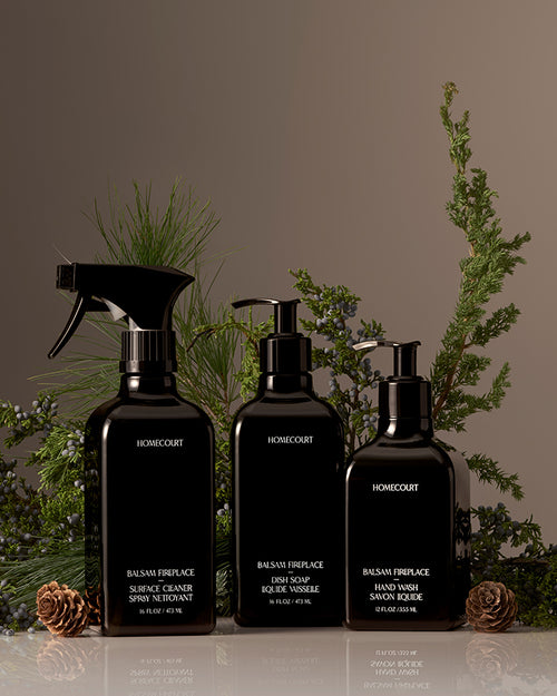 Front view of three Homecourt kitchen cleaning bottles, one spray and two pump dispensers, styled with balsam sprigs and pinecones
